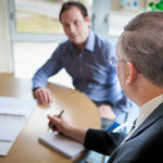 Two business men talking at desk with one making notes