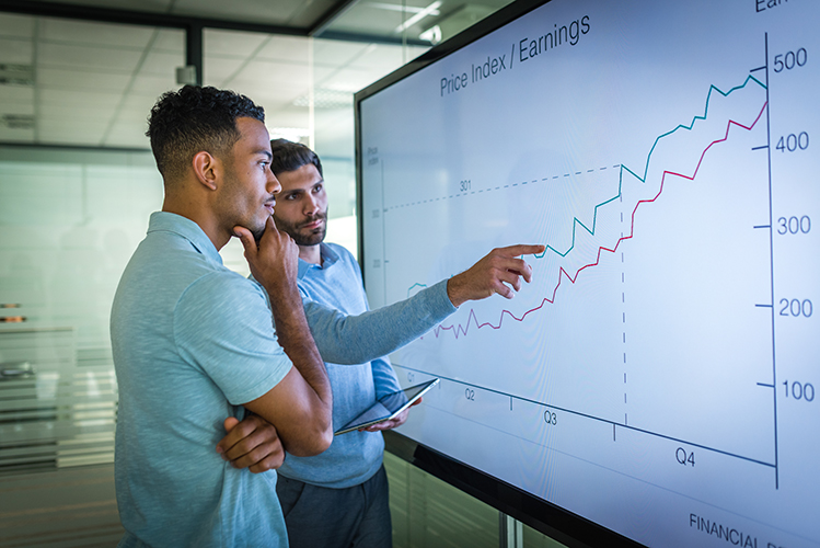 Two men looking at large screen with image of a price graph