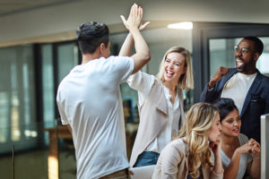 Shot of a group of colleagues giving each other a high five while using a computer together at work