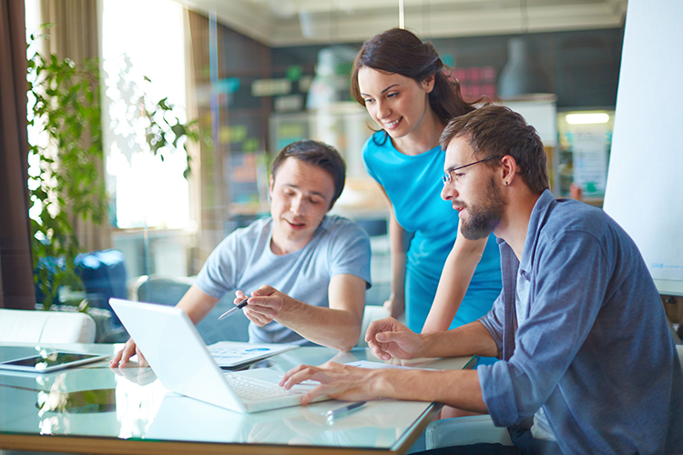 Two men and one woman looking at a laptop on desk