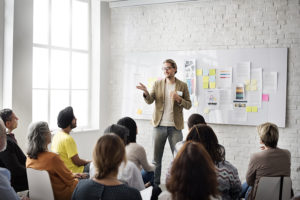 Man presenting to room of people sitting on chairs