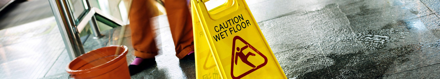 Person cleaning floor with bucket and mop with a wet floor sign