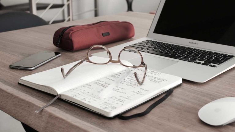 Glasses, phone, pencil case, notepad and laptop on desk