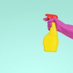 Hand wearing pink glove holding yellow spray bottle