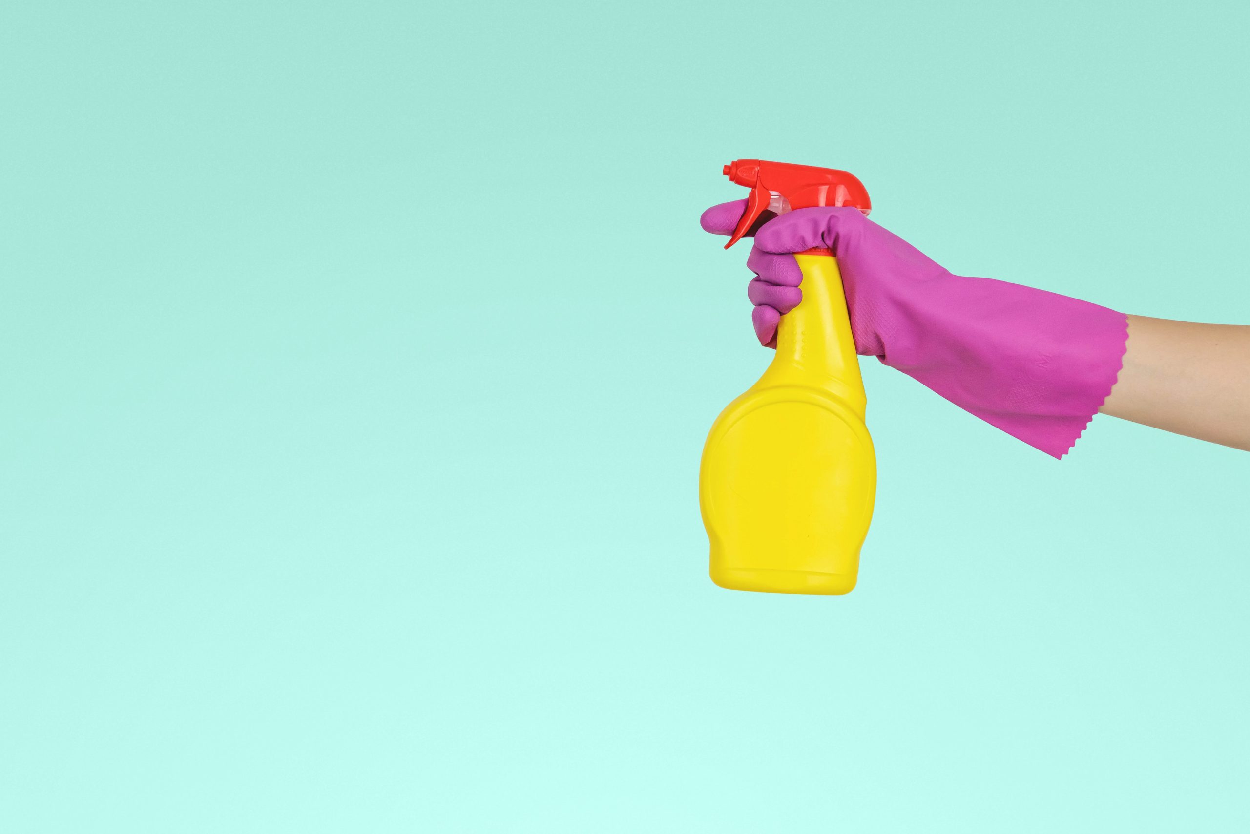 Hand wearing pink glove holding yellow spray bottle