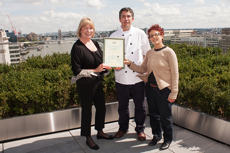 Two women and a man holding a certificate in a rooftop garden